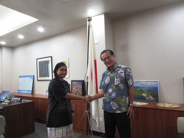 Ambassador Horie and Ms. Katchugo shake their hands in front of Japanese flag